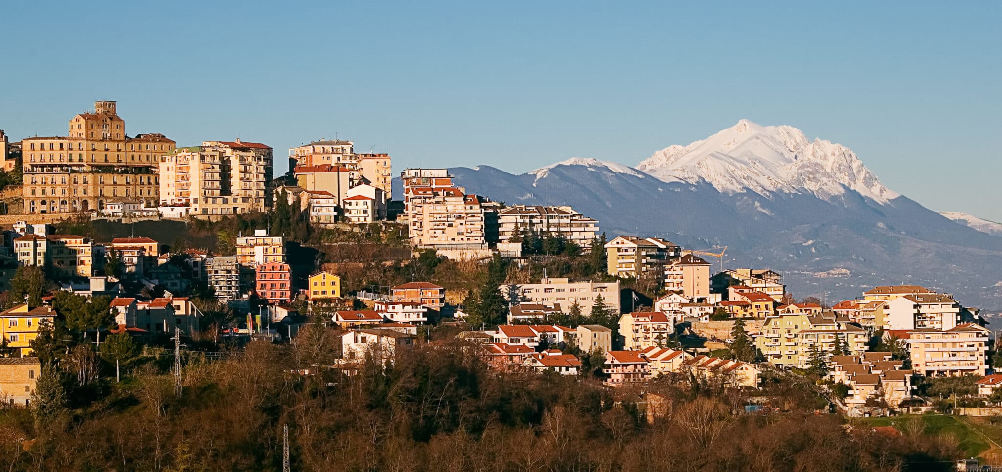 Panorama urbano con montagne innevate sullo sfondo.