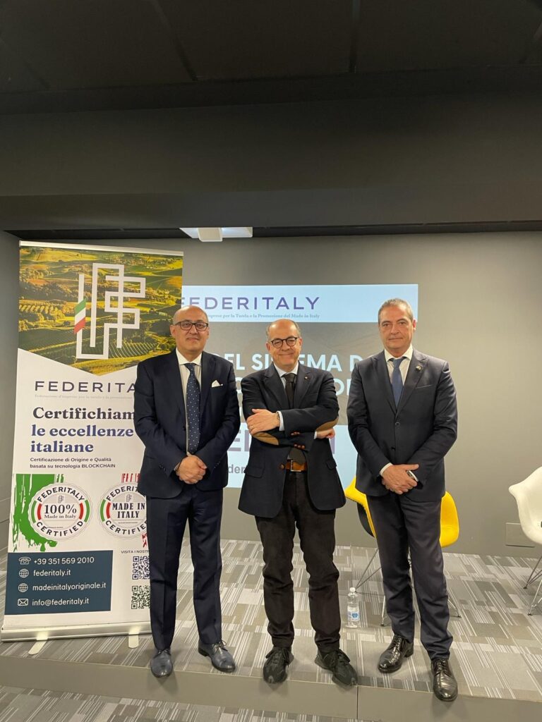 Trio di uomini in abito davanti a banner FEDITALY.