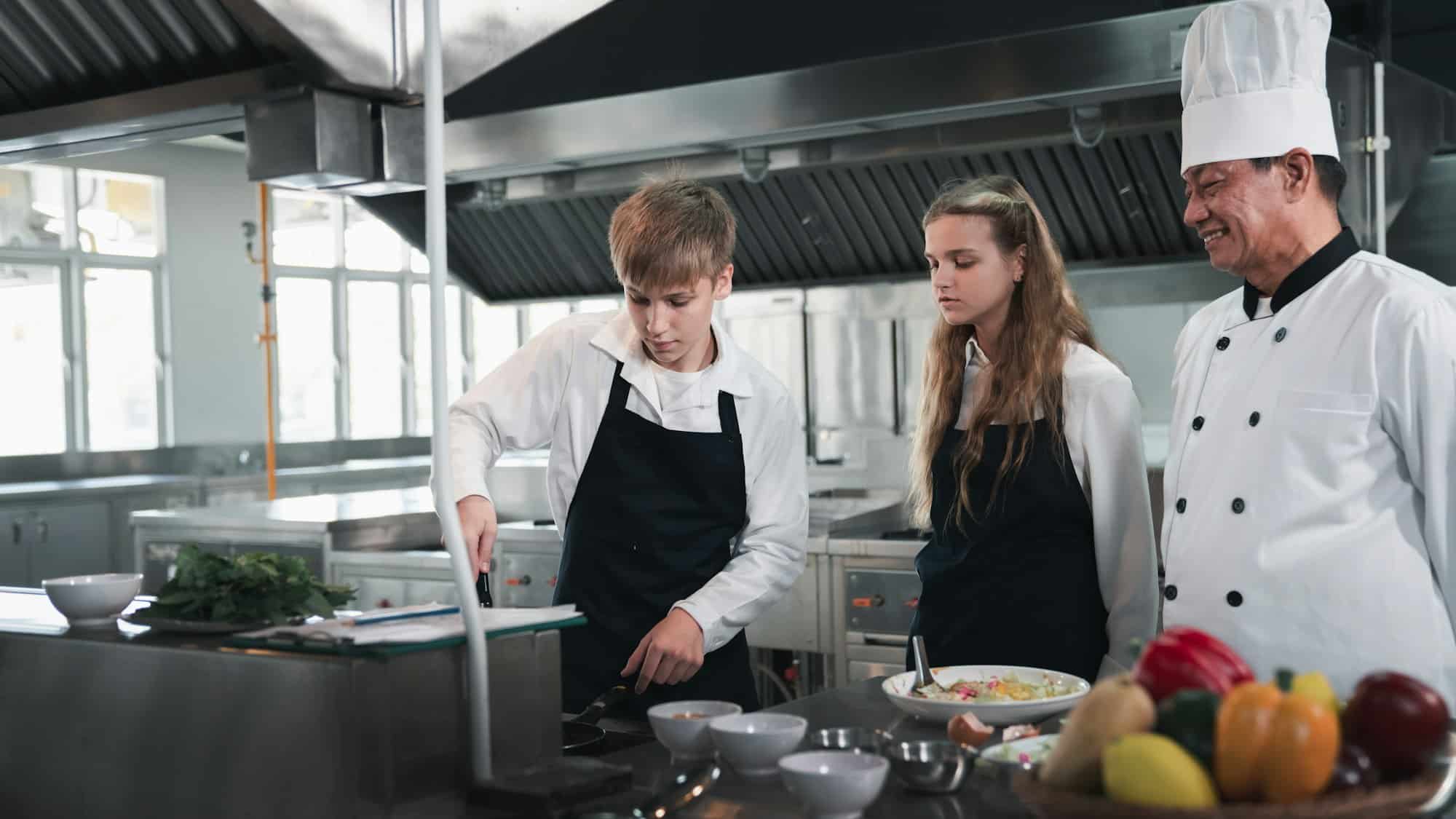 Chef e studenti che cucinano e preparano il cibo in cucina. Lezione di cucina per bambini.