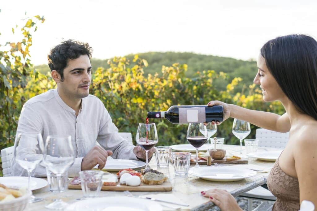 Italien, Toskana, Siena, junges Paar beim Abendessen in einem Weinberg mit Rotwein