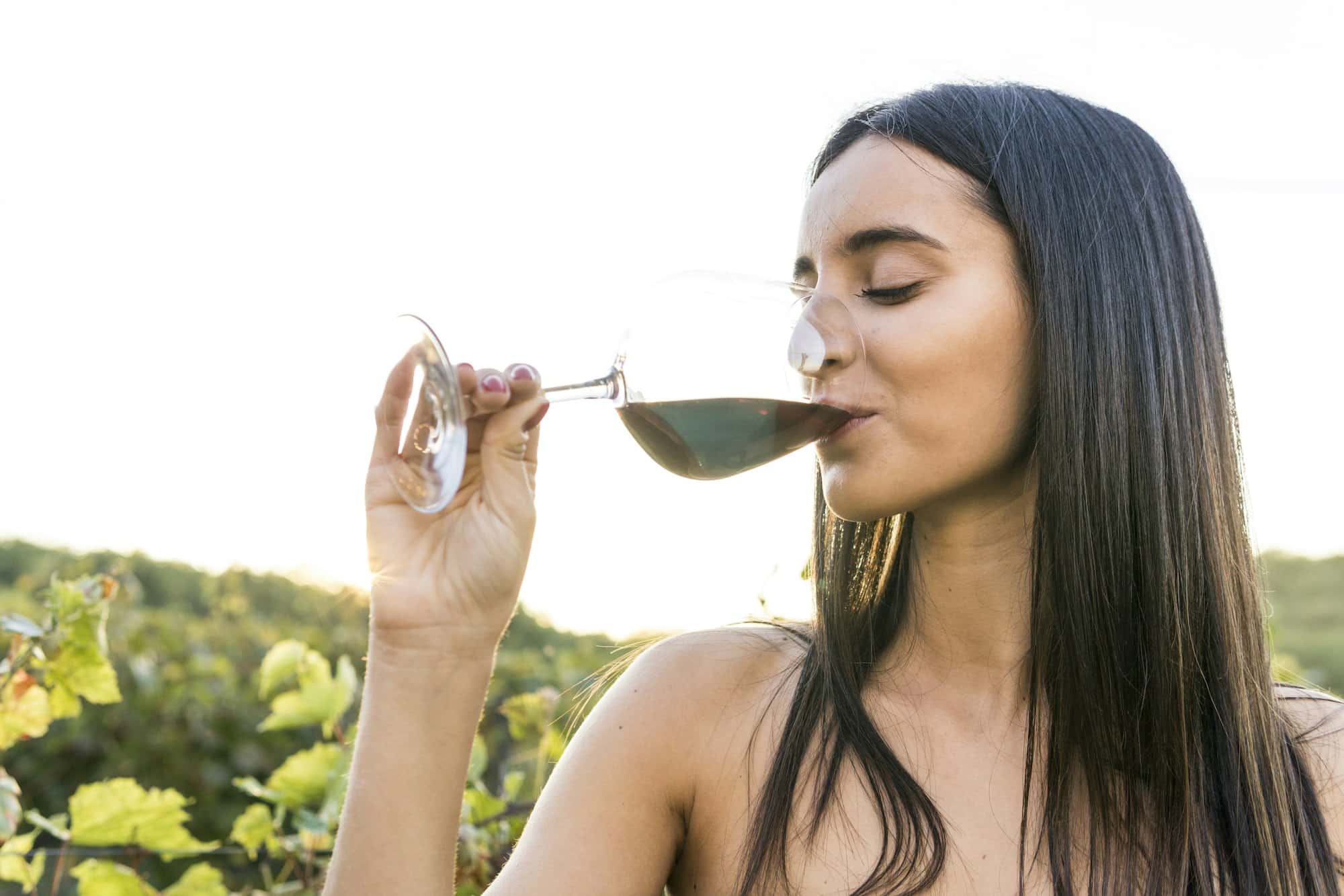 Italia, Toscana, Siena, giovane donna che beve vino rosso in un vigneto al tramonto