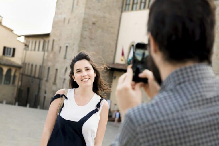 Over shoulder view of man photographing girlfriend by Arezzo Cathedral, Arezzo, Tuscany, Italy