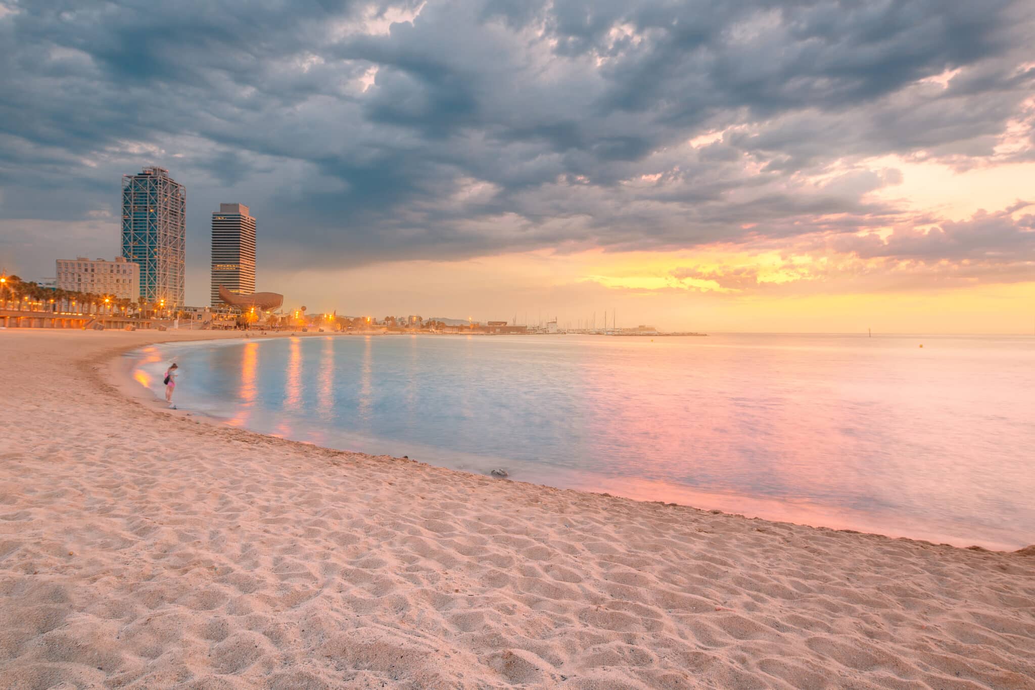 Spiaggia al tramonto con grattacieli e cielo nuvoloso.