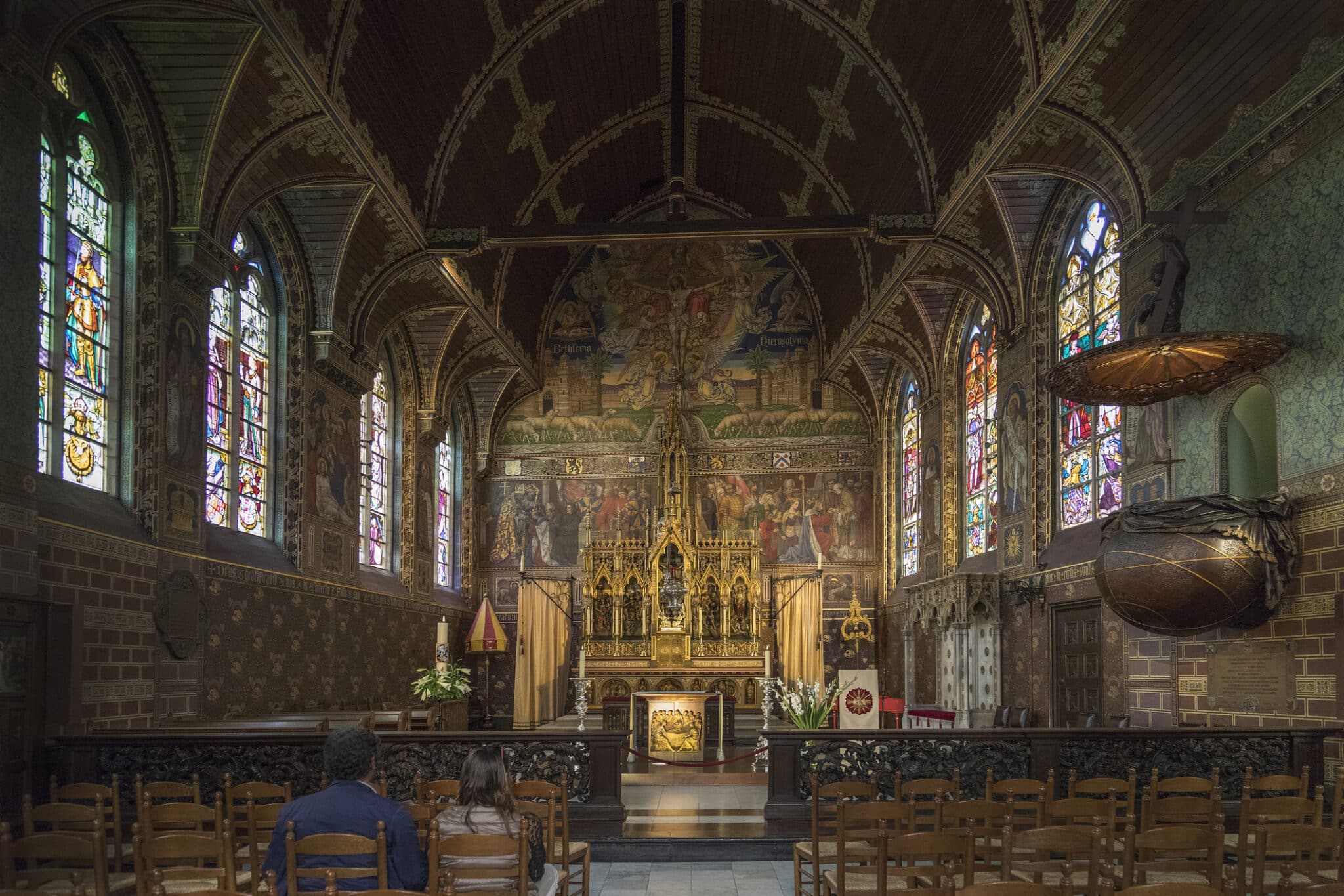 Intérieur d'église gothique, vitraux, fresques, fidèles assis.