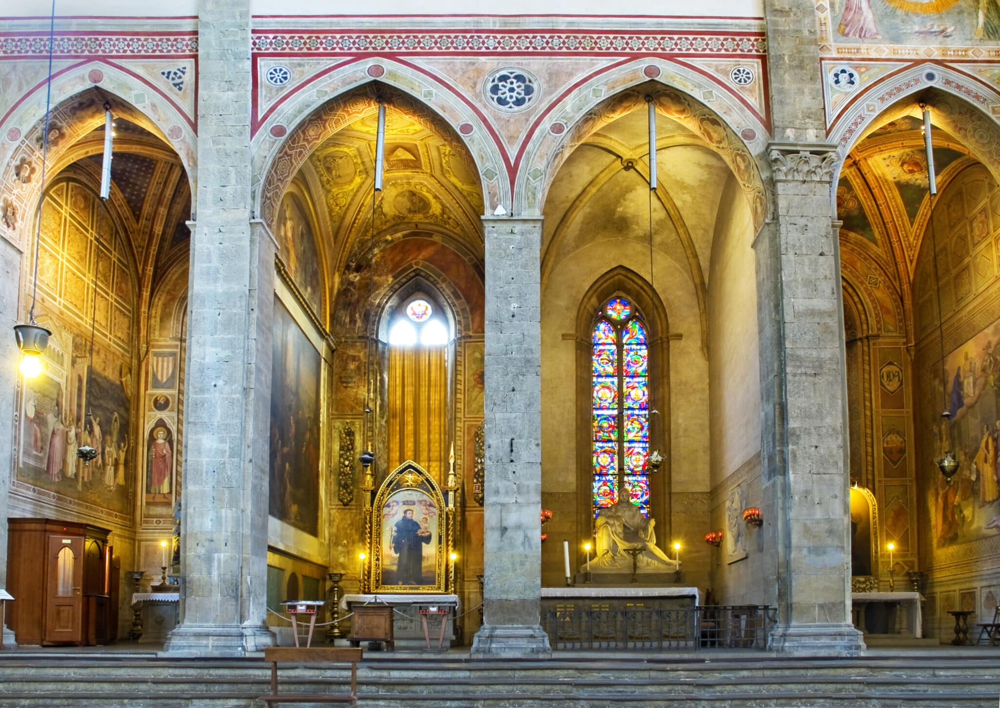 Interno chiesa gotica con affreschi e vetrate colorate.