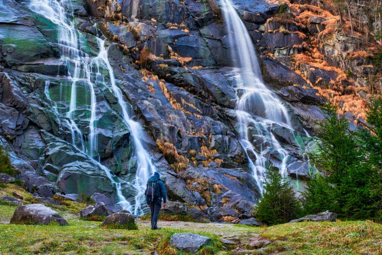 Hiker in front of mountain waterfall.