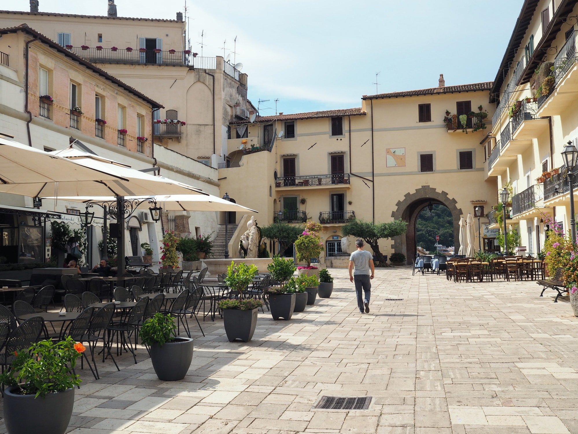 Piazza italiana con caffè all'aperto e passante.