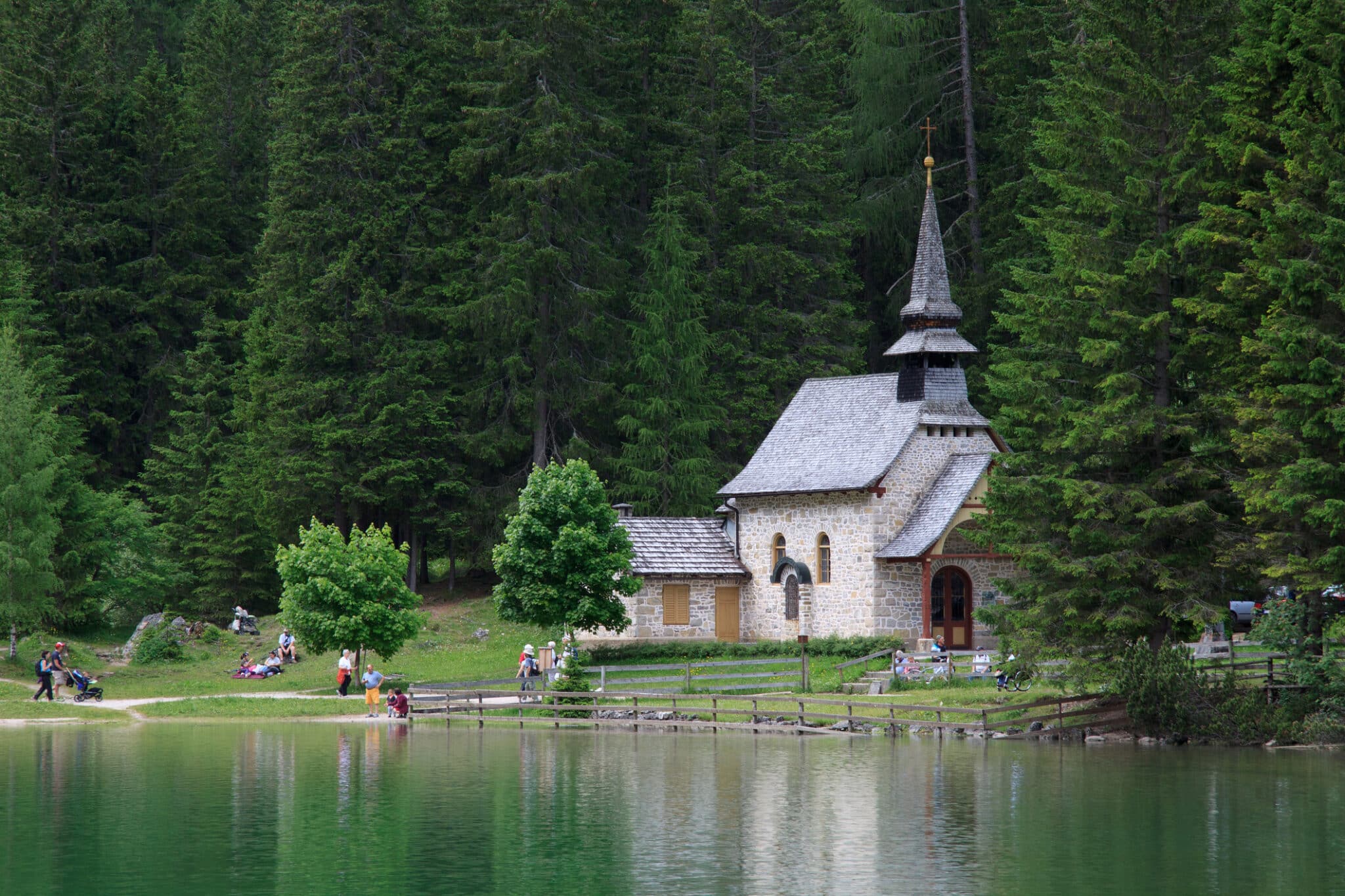 Chiesetta alpina accanto a lago e pini.