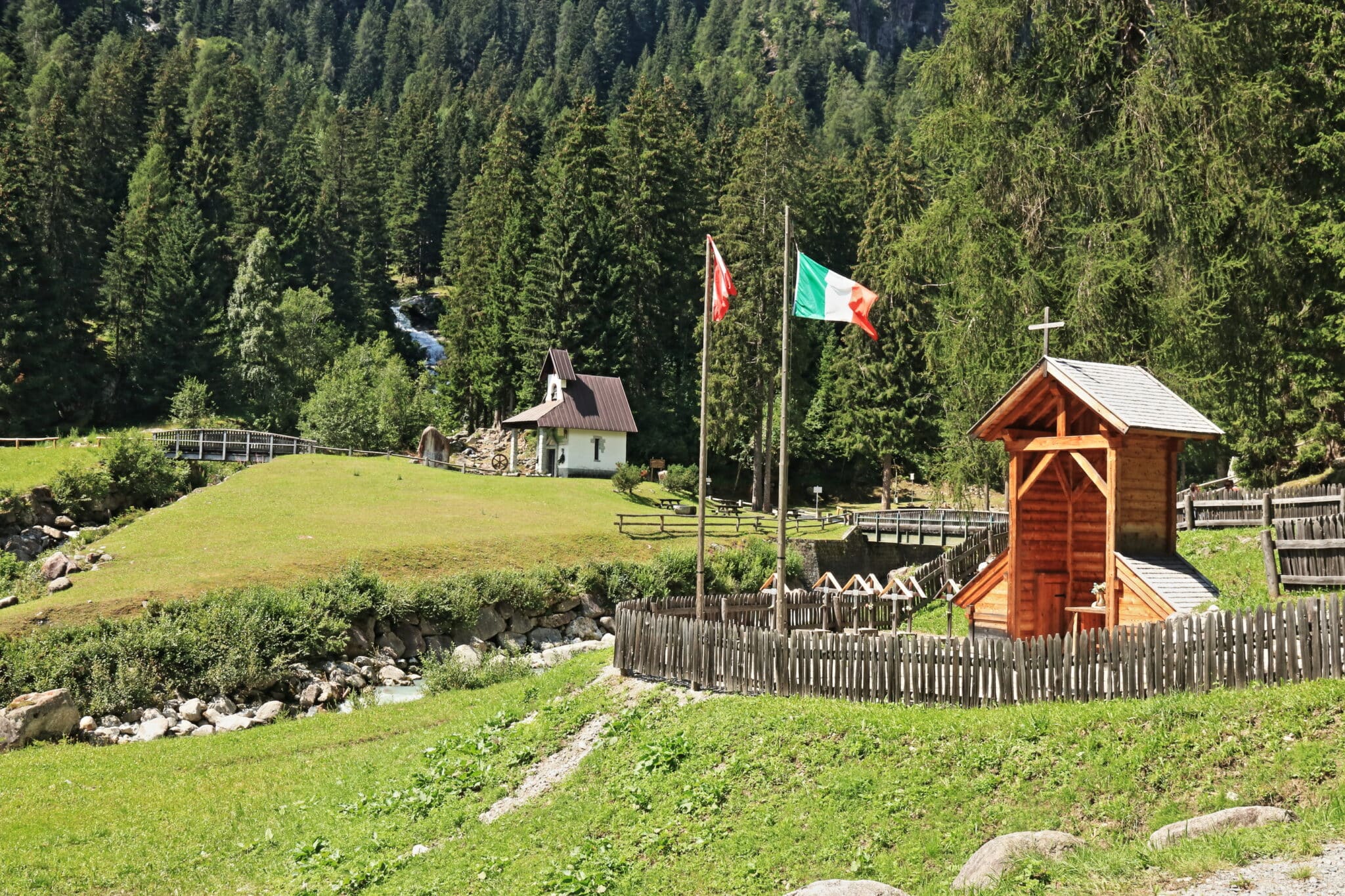 Paesaggio montano italiano con chiesetta e bandiere.