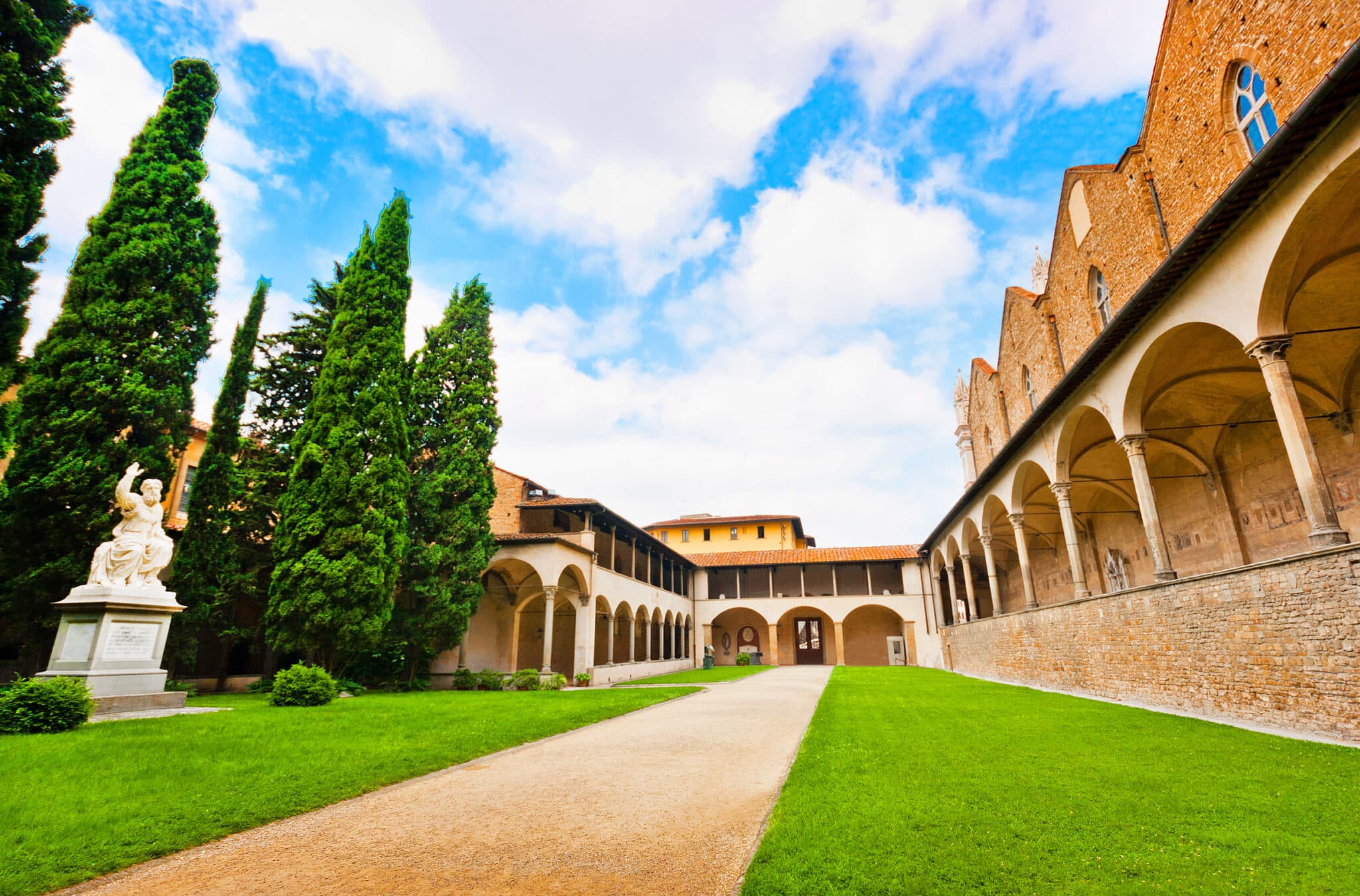 Chiostro medievale con statue e cipressi.