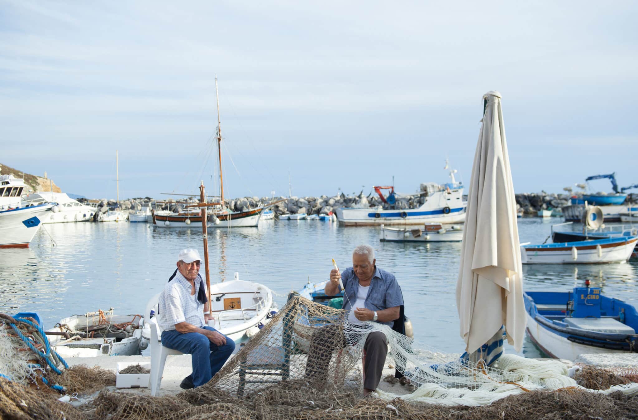 Due vecchi pescatori con rete da pesca nel porto dell'isola di Procida vicino Napoli, Italia meridionale