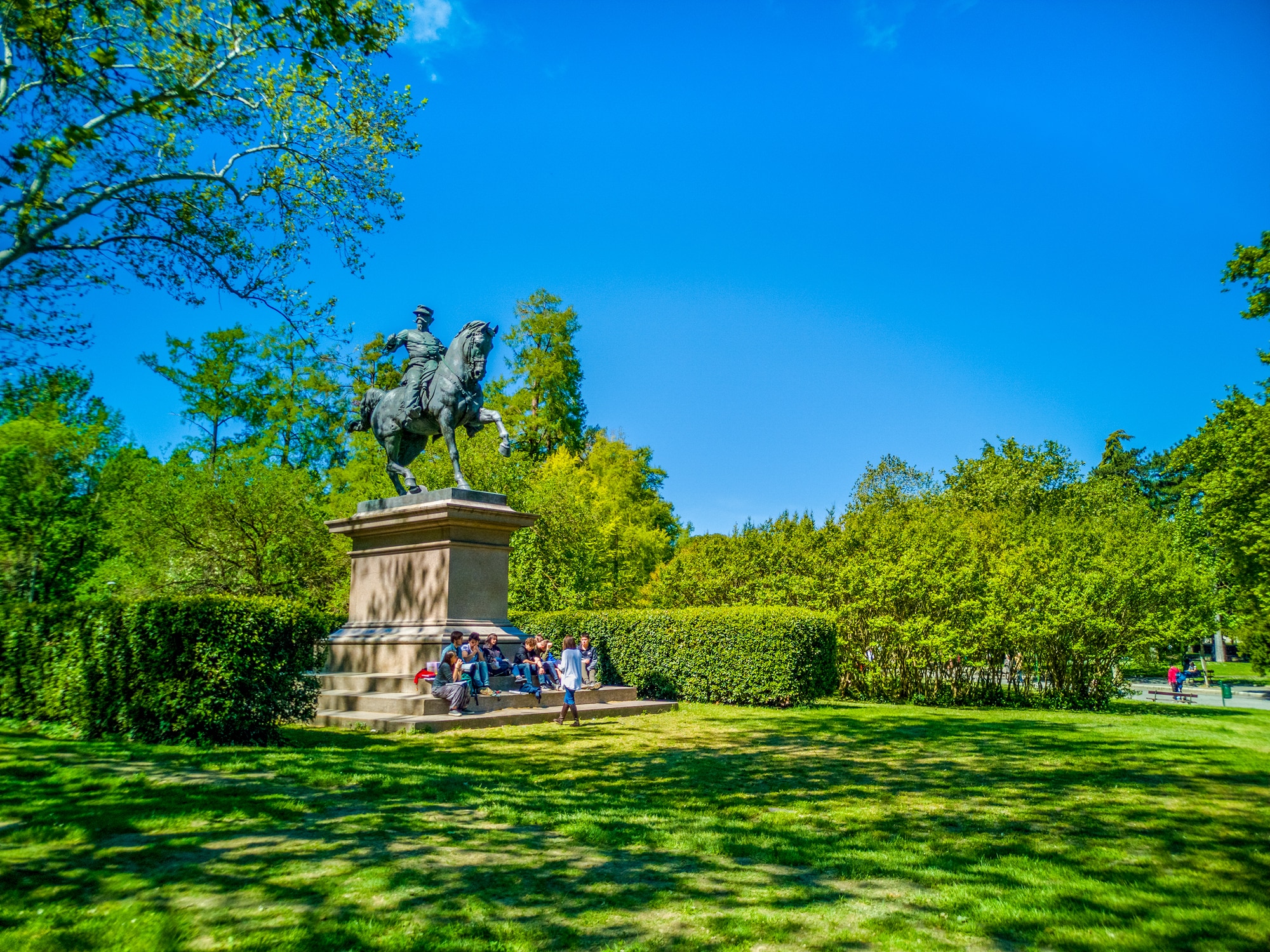 Statue équestre dans un parc ensoleillé avec des gens.