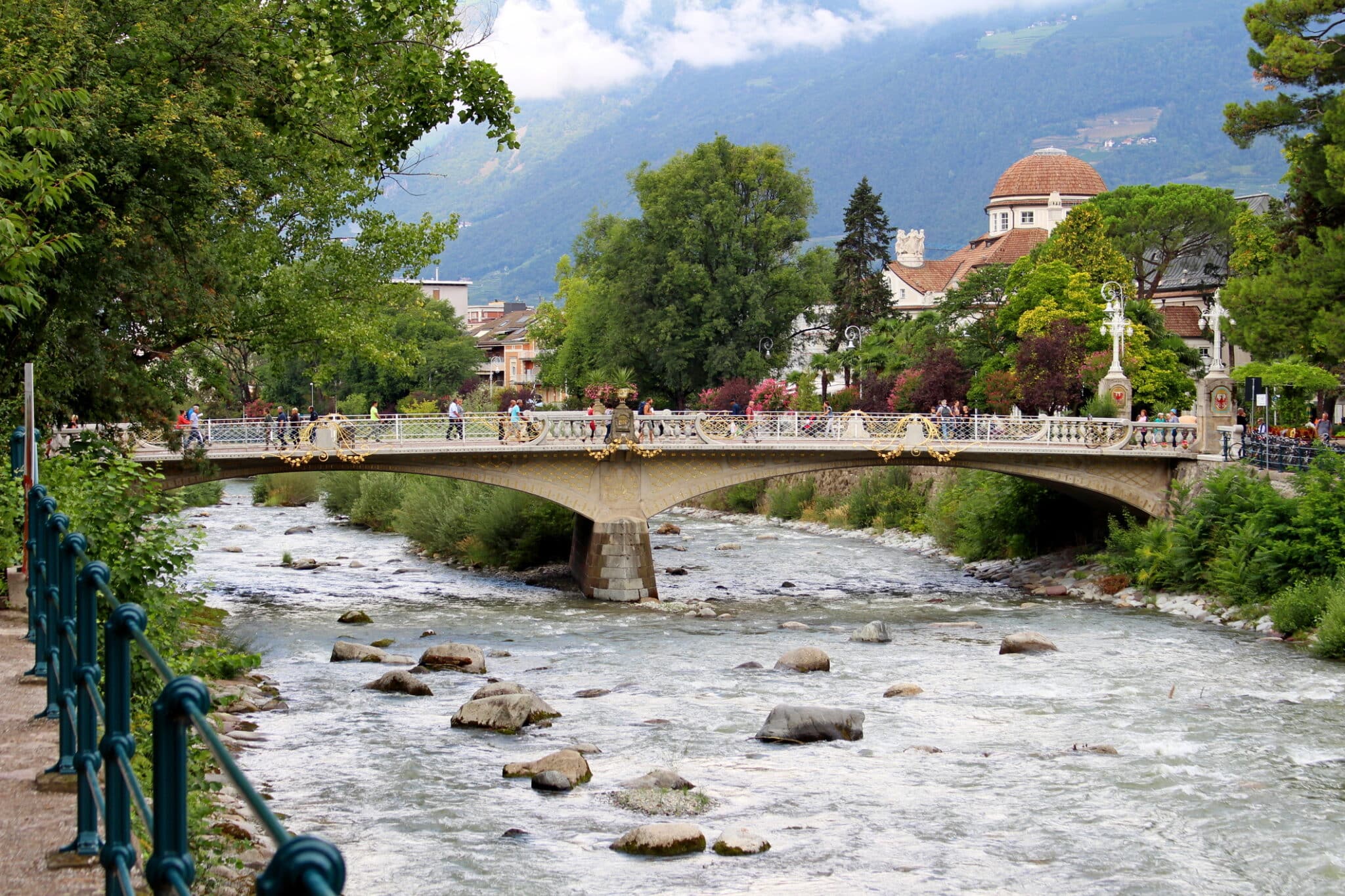 Ponte cittadino su fiume con persone e vegetazione.