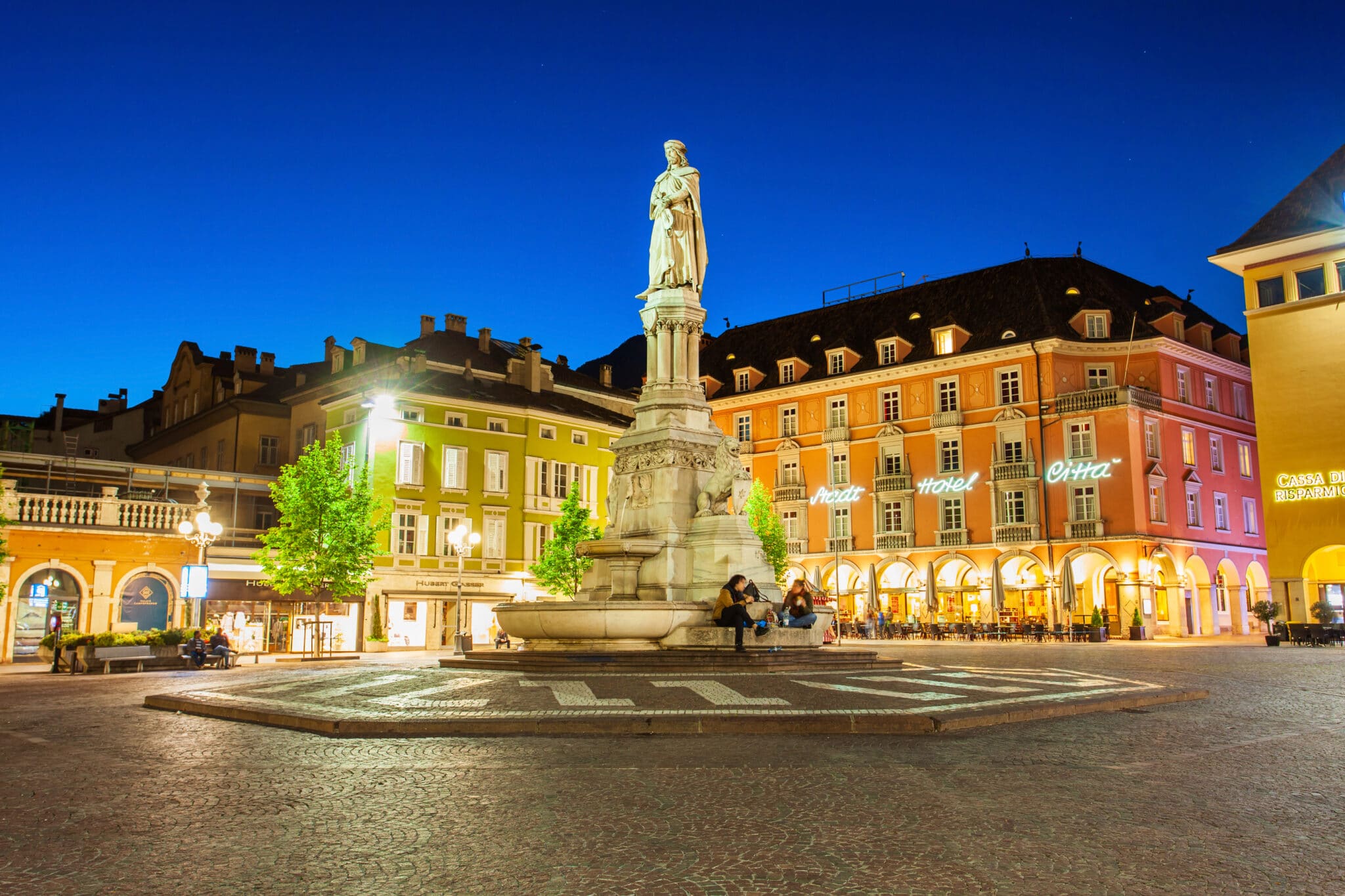 Piazza serale con monumento e edifici colorati.