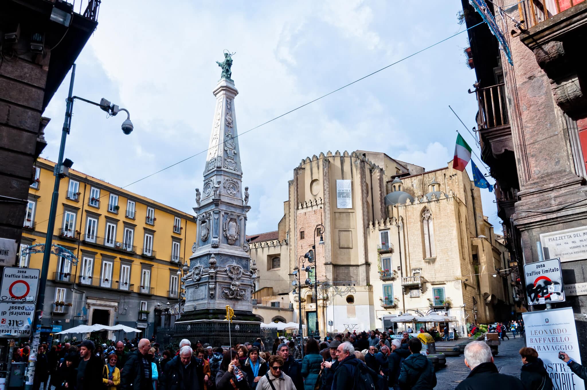 Piazza affollata con monumento e bandiere italiane.