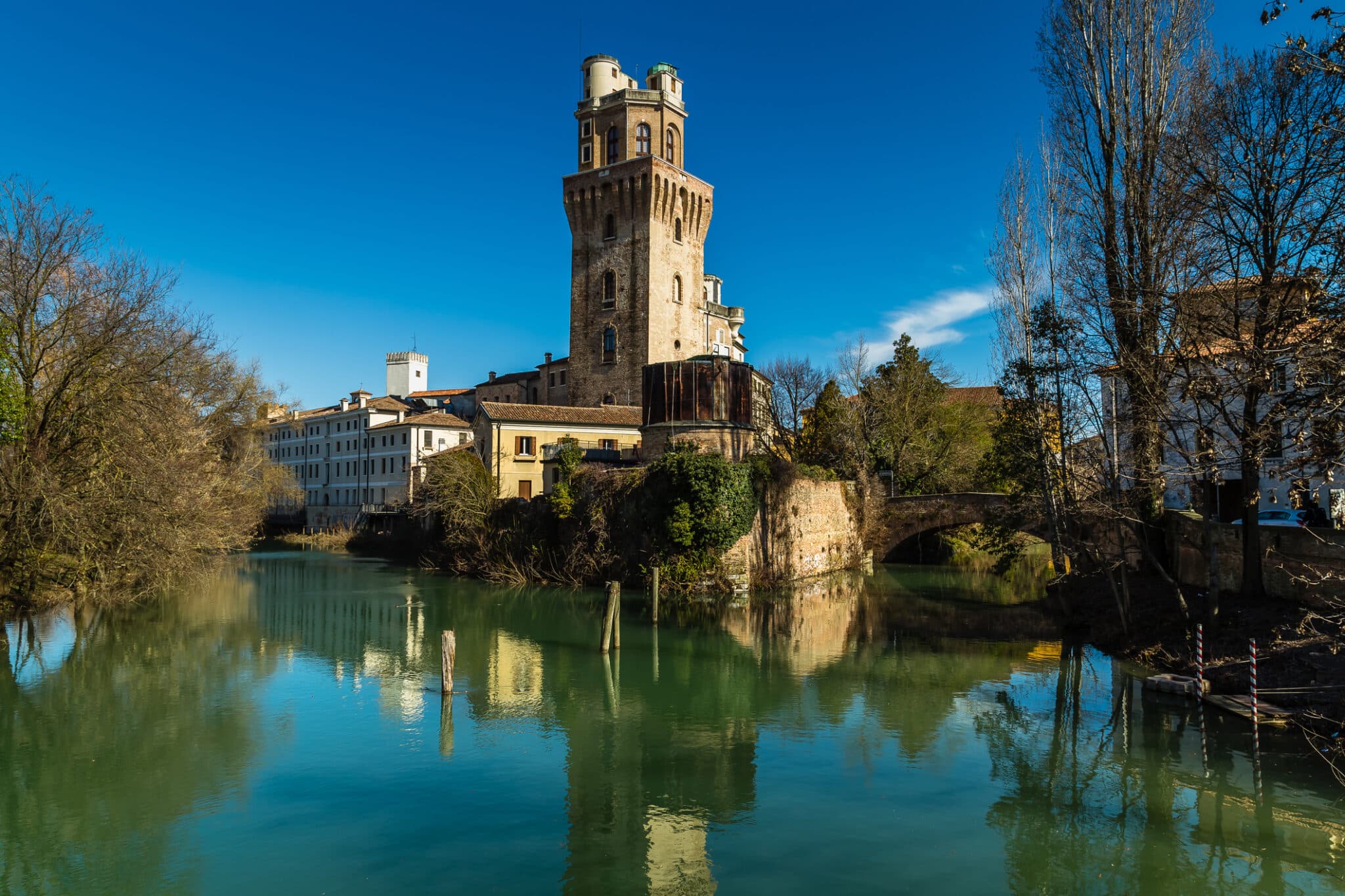 Torre medievale riflessa in fiume soleggiato.