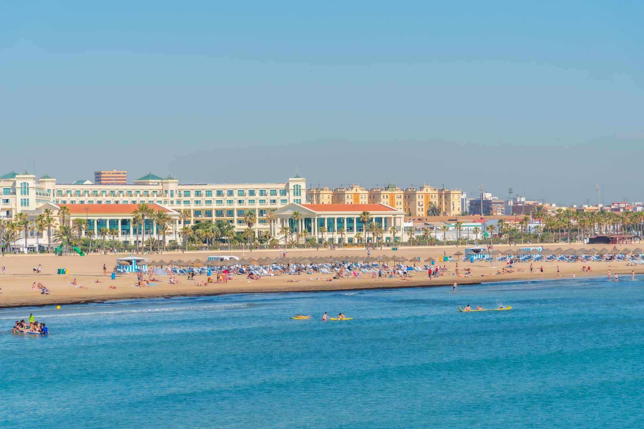 Spiaggia affollata con palme e hotel.