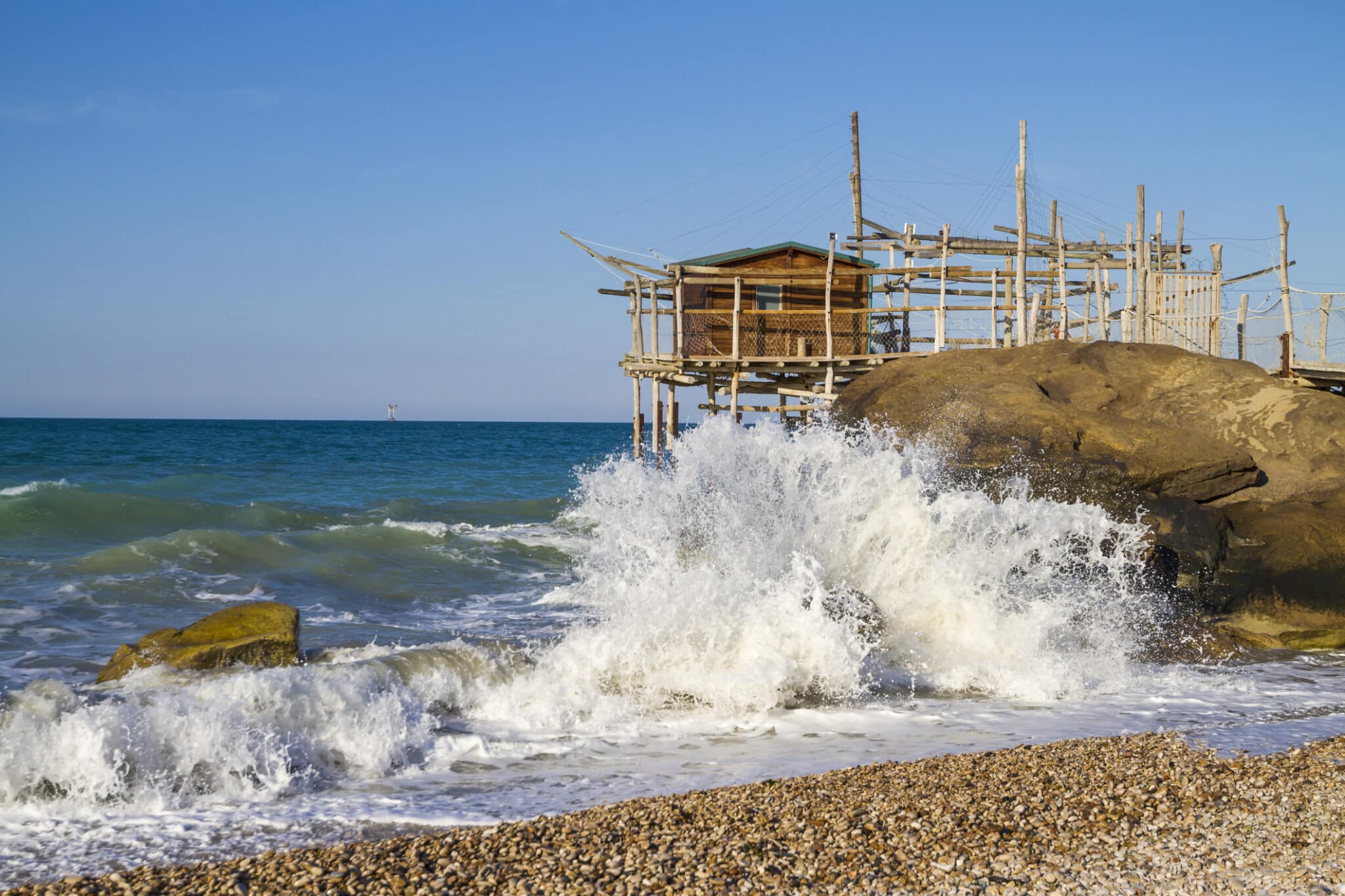 Trabocco in legno su mare con onde e ciottoli.