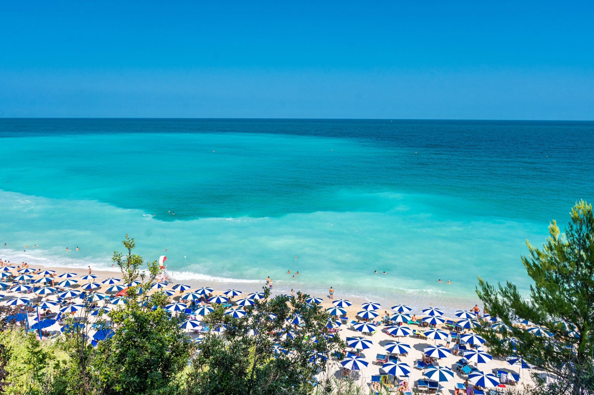 Spiaggia affollata con ombrelloni e mare turchese.