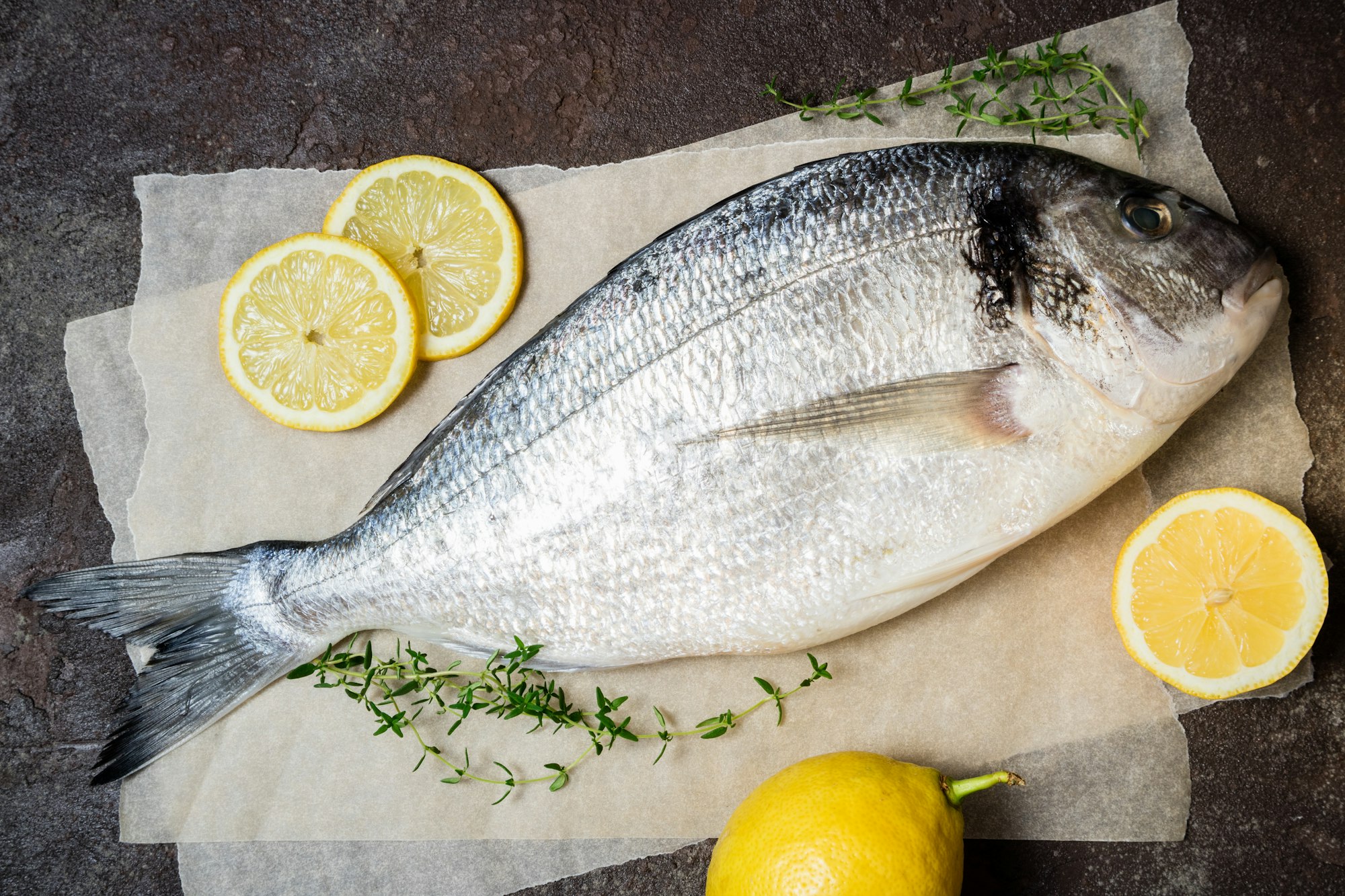 Primo piano del pesce crudo fresco. Pesce Dorado con limone ed erbe aromatiche sul tavolo della cucina. Cucinare il pesce