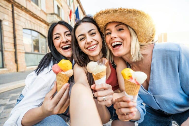 Trois adolescentes enjouées mangeant des cornets de glace dans une rue de la ville