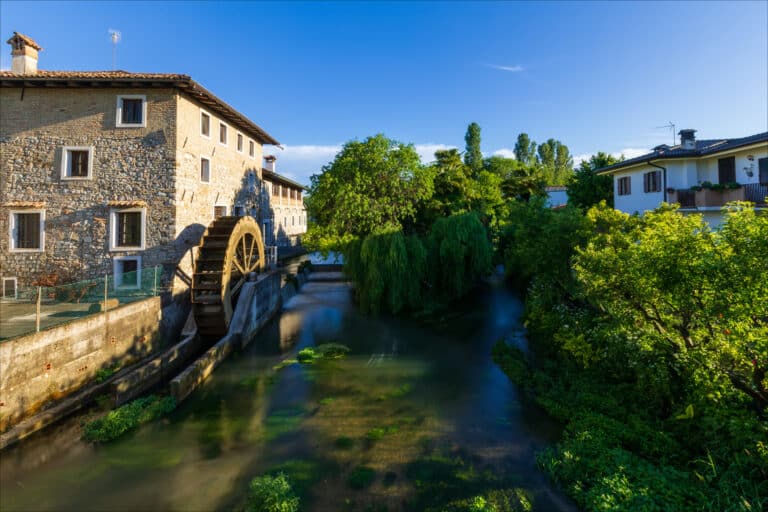 Old paddle mill on the river in the medieval village of Strassoldo. Italy. One of the most beautiful villages in Italy. Wild vegetation.