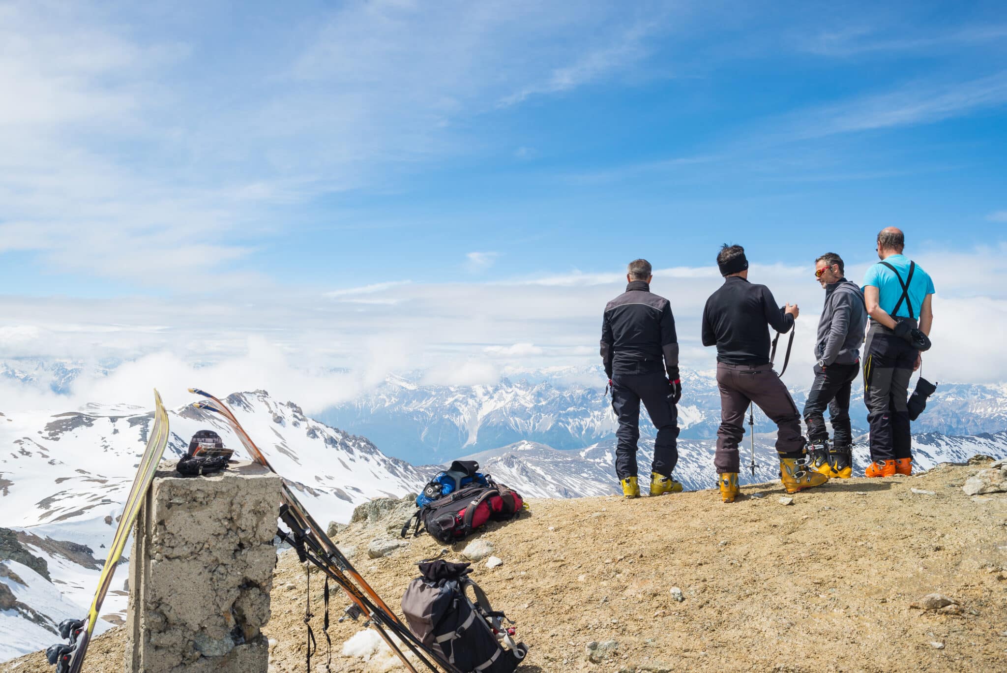 Gruppo di quattro alpinisti che chiacchierano sullo sfondo panoramico di alta quota sulla vetta del M. Sommeiller 3333 m nelle Alpi francesi italiane in una giornata soleggiata di primavera.