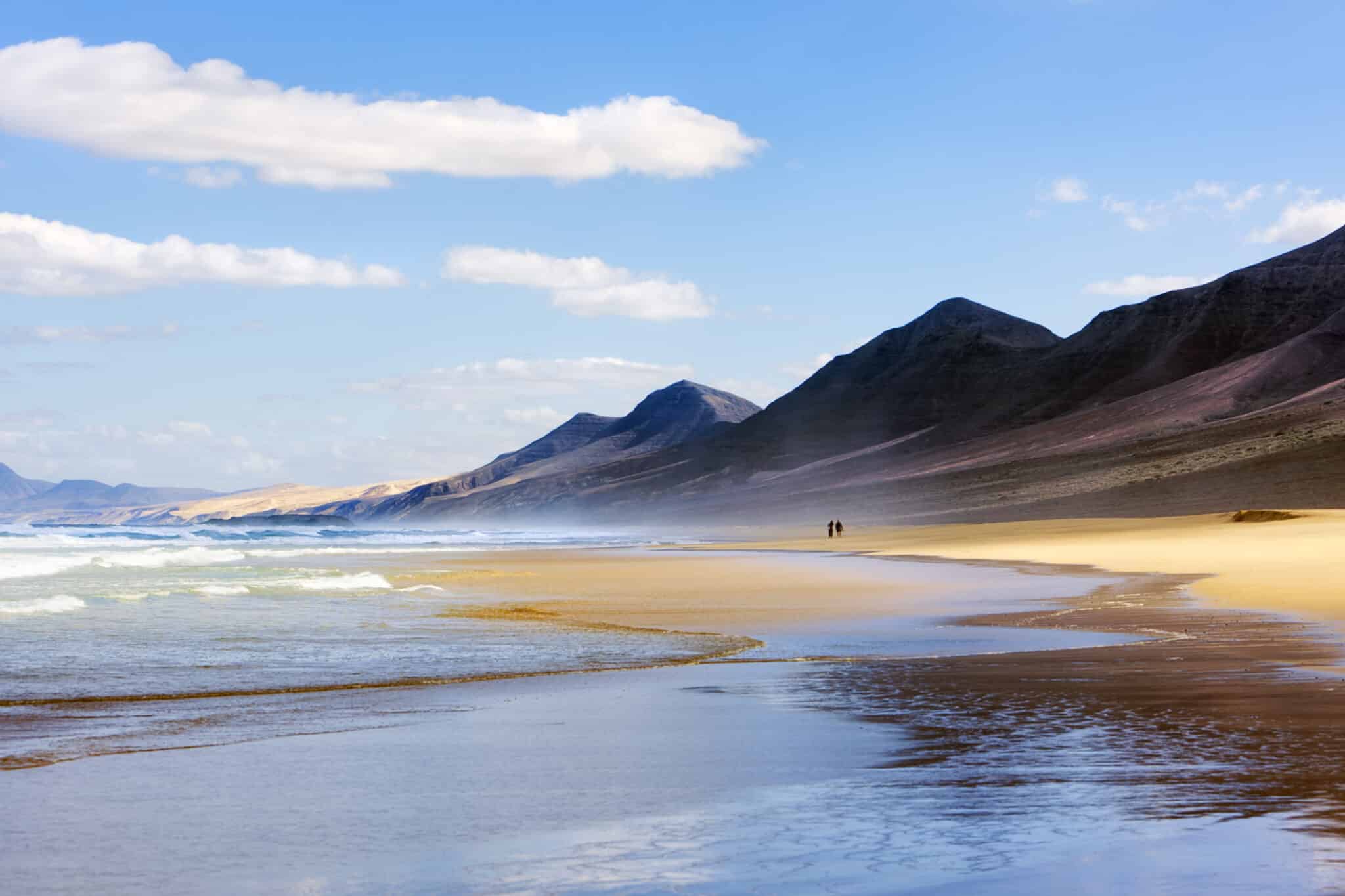 Spiaggia di Cofete, Fuerteventura. Due persone che camminano tra gli spruzzi dell'Oceano Atlantico sulla spiaggia solitaria di Cofete