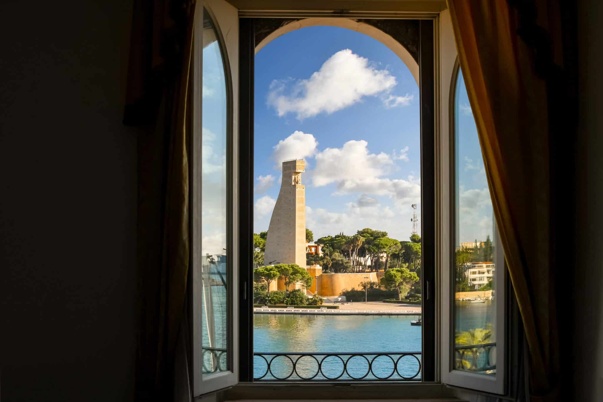 Vista del mare, del paesaggio e del Monumento ai Marinai Italiani attraverso una finestra ad arco in una giornata di sole nel porto di Brindisi, Italia.