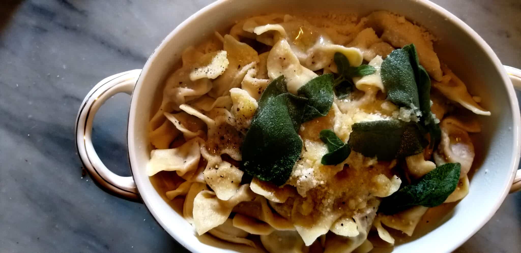 Tortellini au beurre et à la sauge dans un plat blanc.