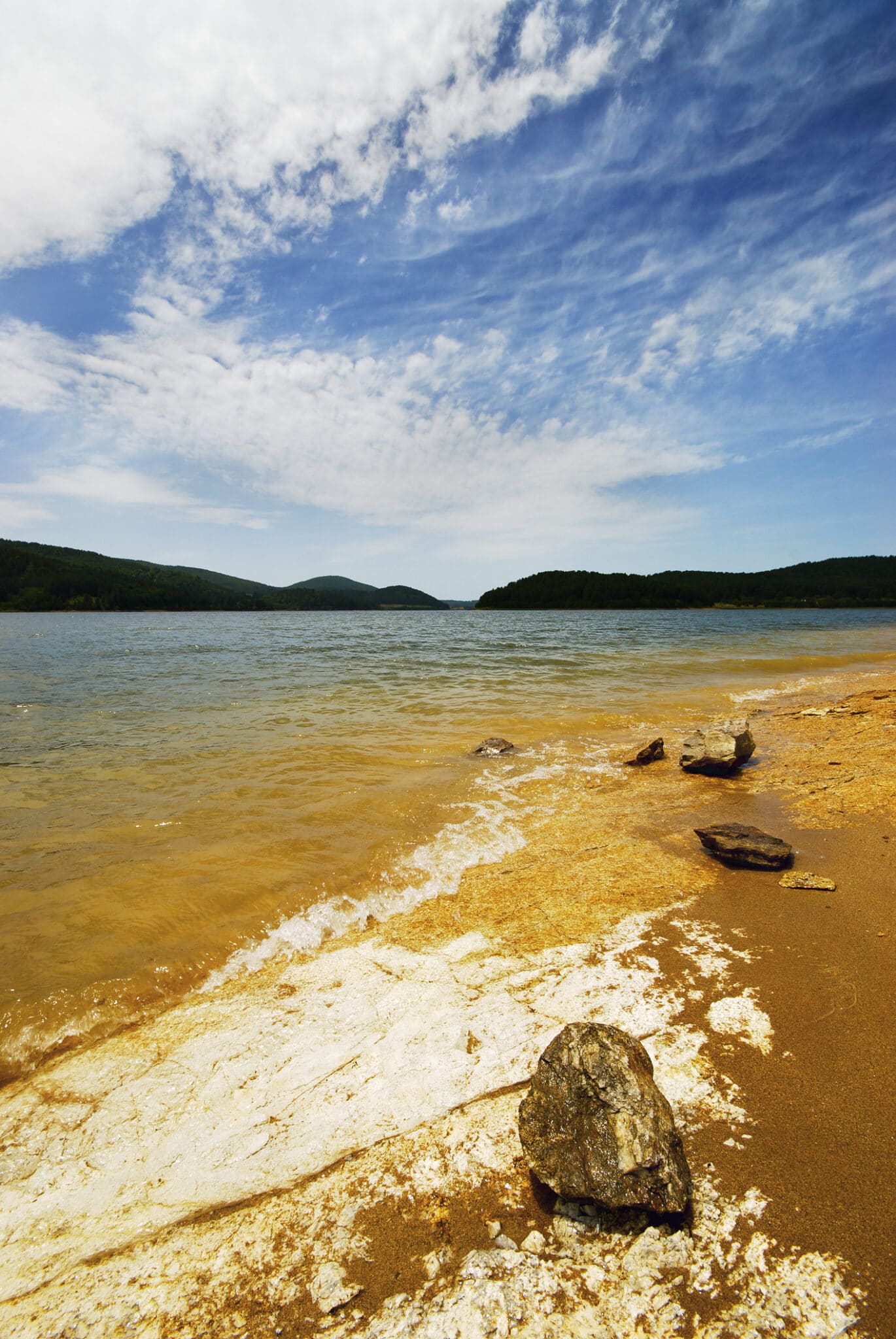 Plage de sable et de pierre, lac et ciel bleu.