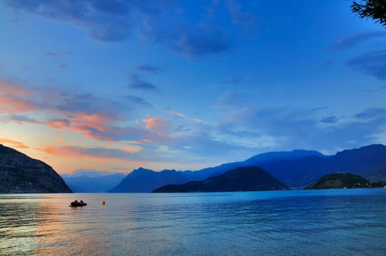 Coucher de soleil sur le lac avec bateau et montagnes.