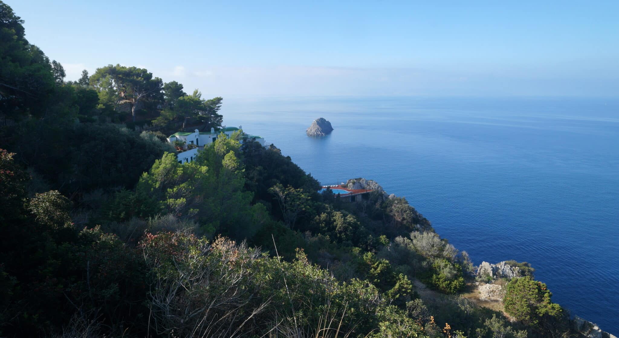 Vista mare con scogli e vegetazione lussureggiante.