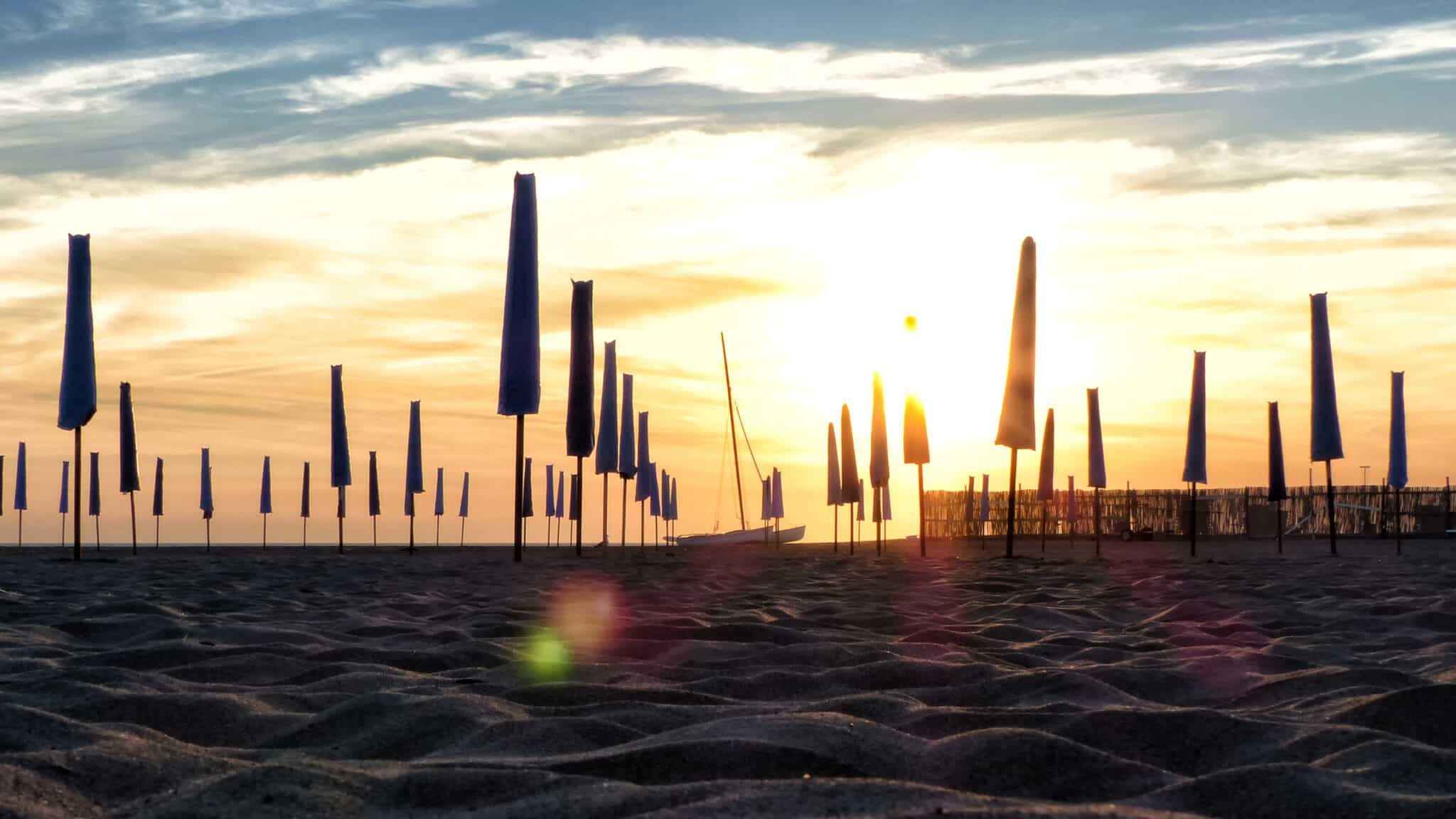 Coucher de soleil avec des parasols fermés sur la plage.