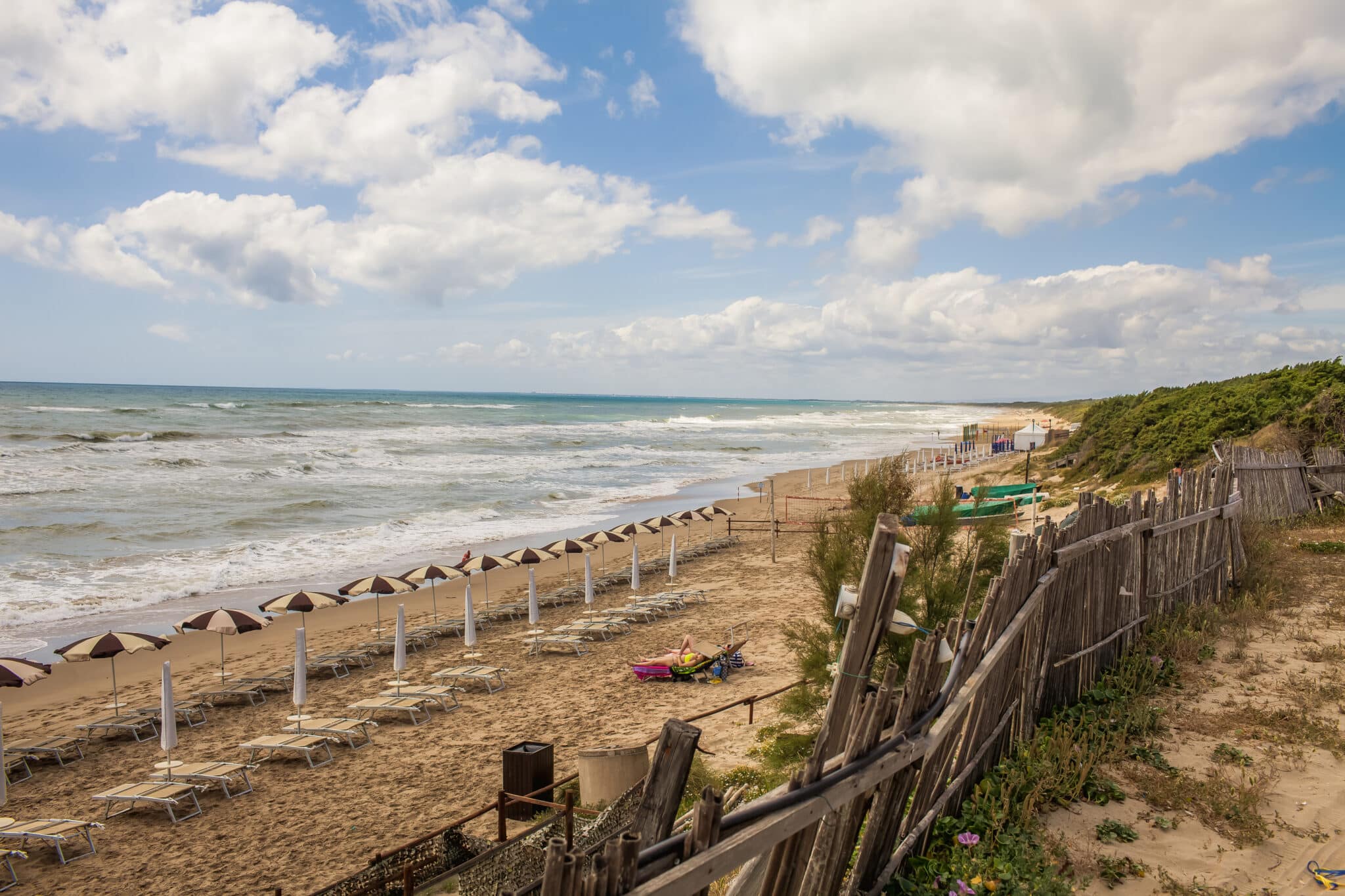 Spiaggia con ombrelloni e lettini, mare e cielo nuvoloso.