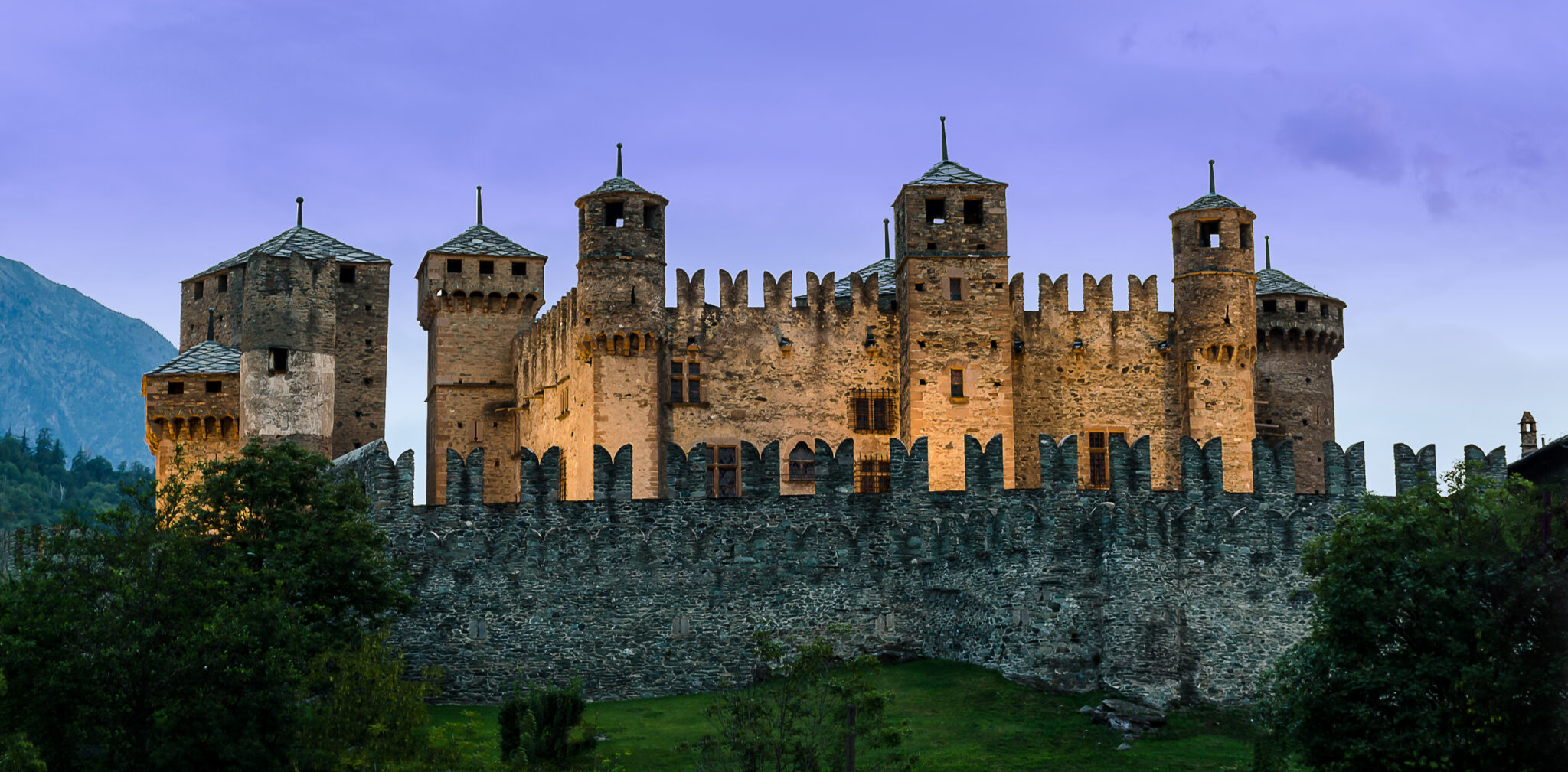 Castello medievale al tramonto con montagne sullo sfondo