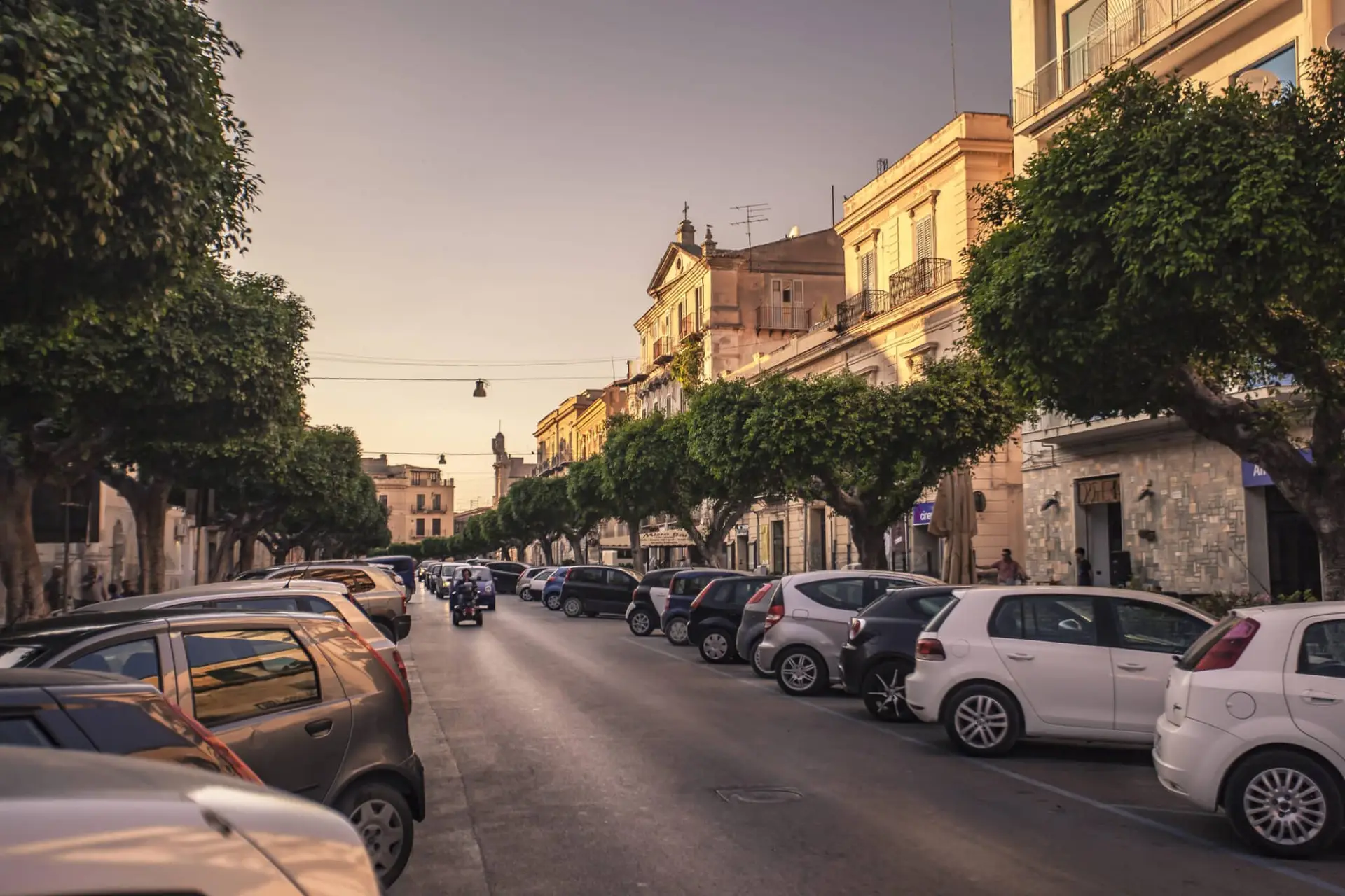 Strada al tramonto con auto parcheggiate e alberi