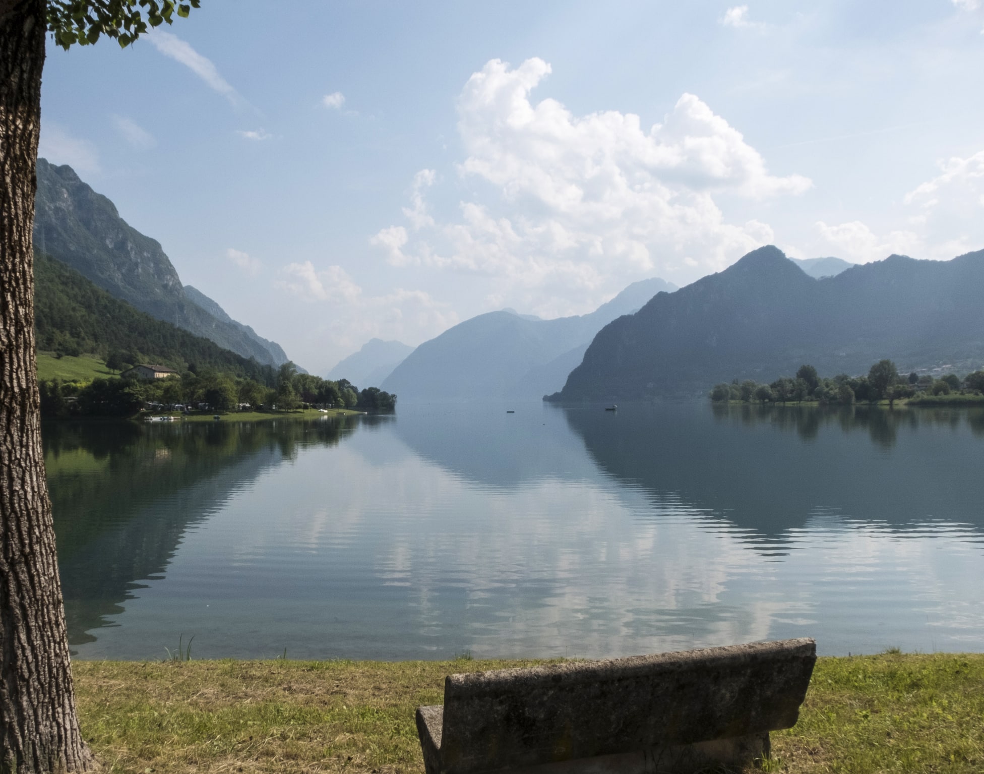 Lago calmo con montagne, alberi e panchina