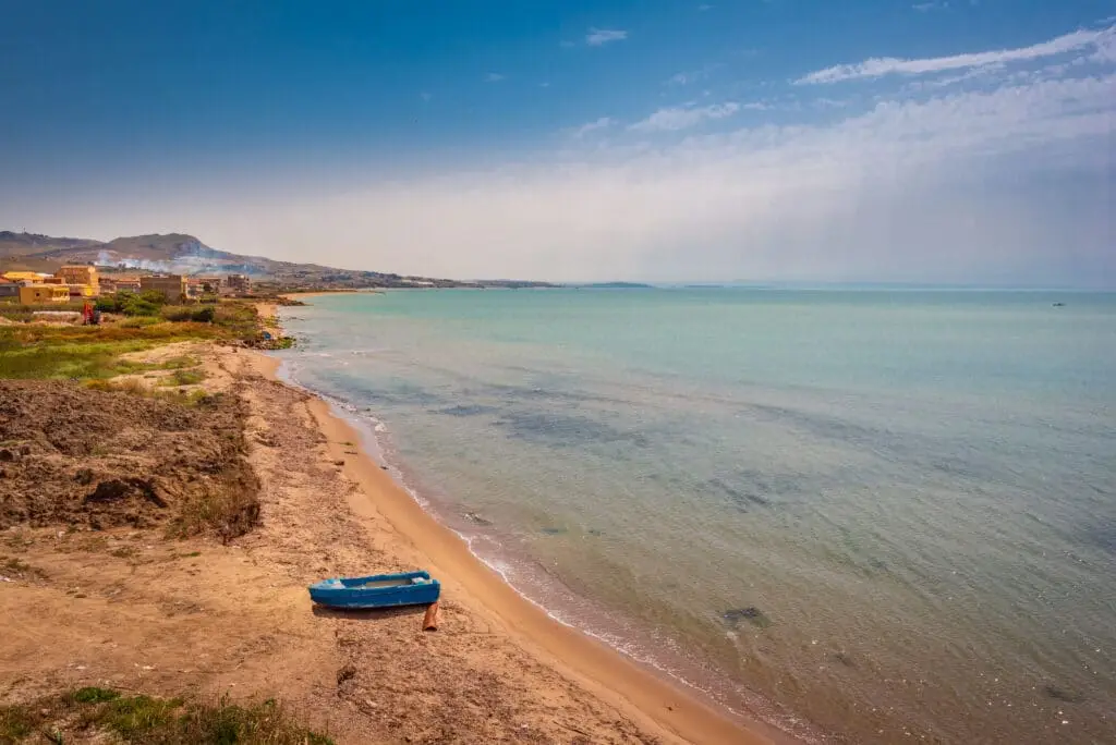 Playa de arena con barco azul, mar en calma, cielo despejado