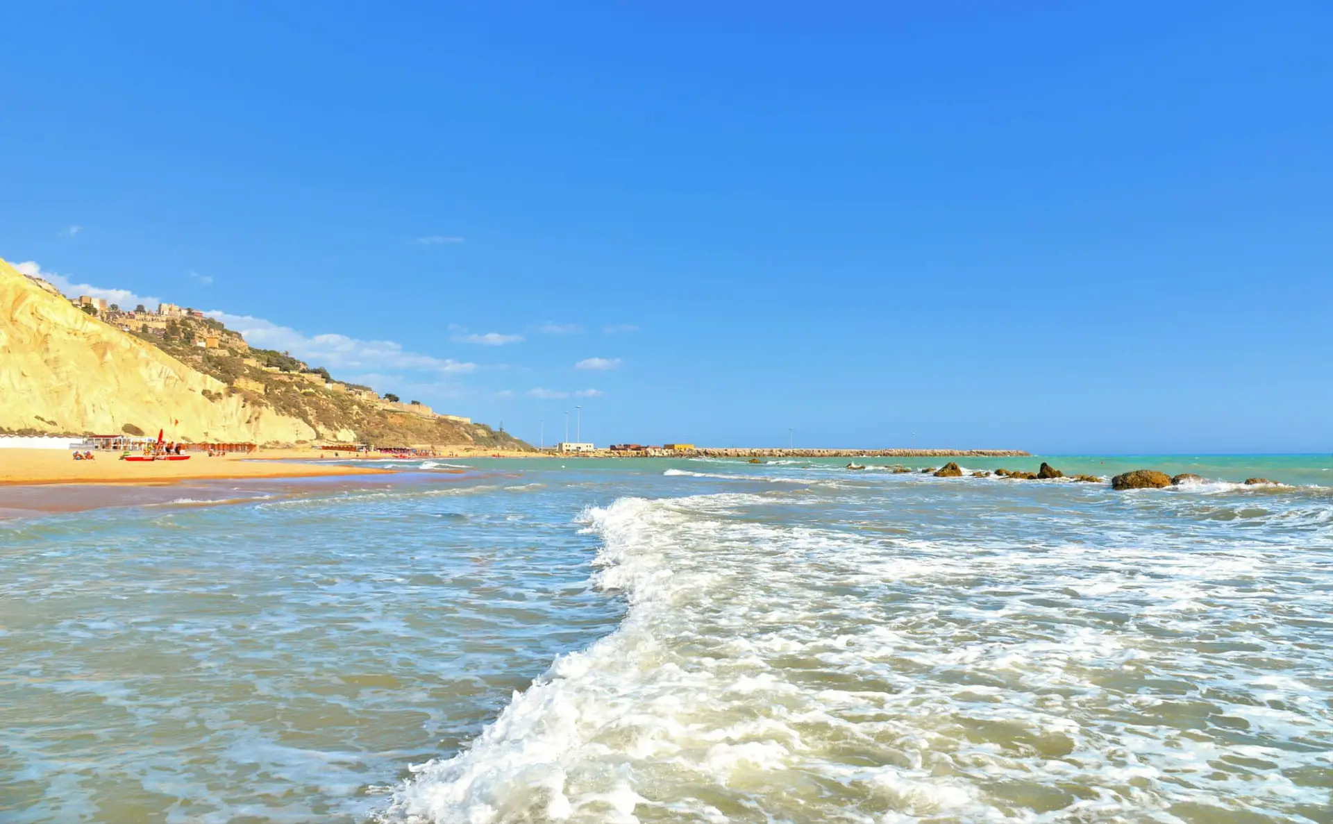 Spiaggia soleggiata con scogliere e mare agitato