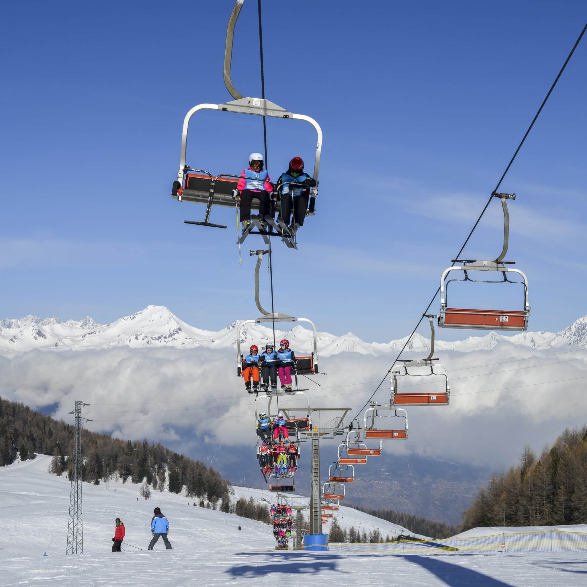 Sciatori su seggiovia con montagne innevate