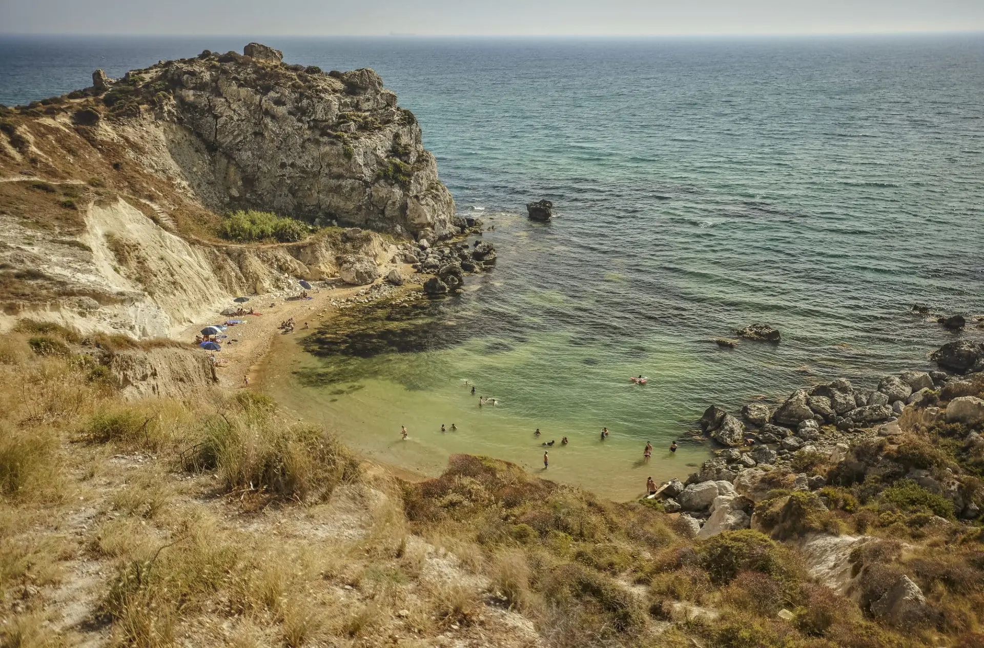 Caletta rocciosa con bagnanti e ombrelloni, mare verde