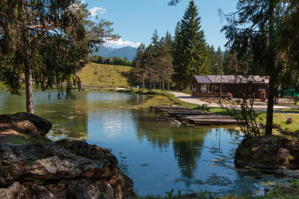 Bergsee mit Spiegelungen, Bäumen und Holzhütte