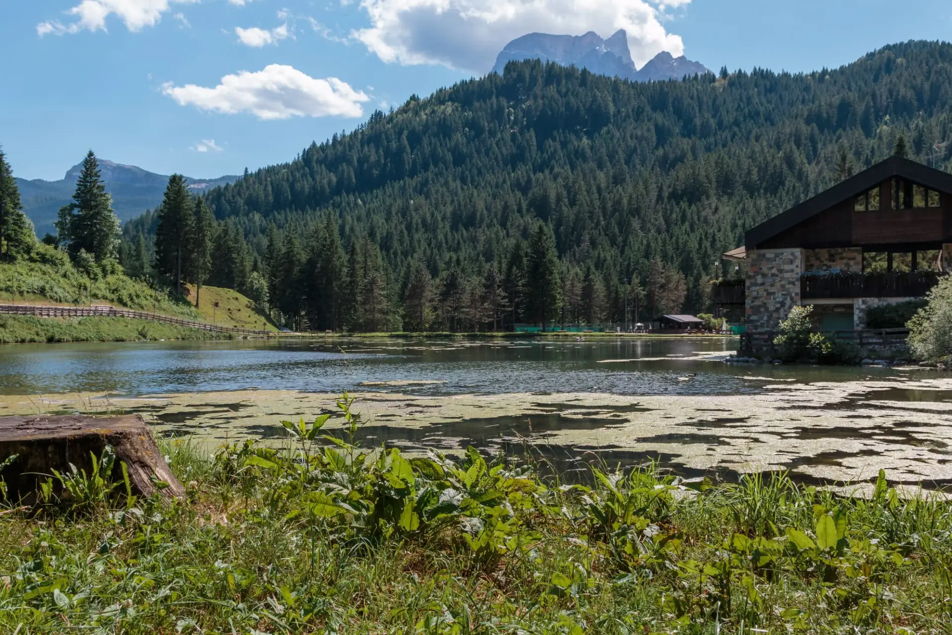 Lago alpino con casa, alberi e montagne sullo sfondo